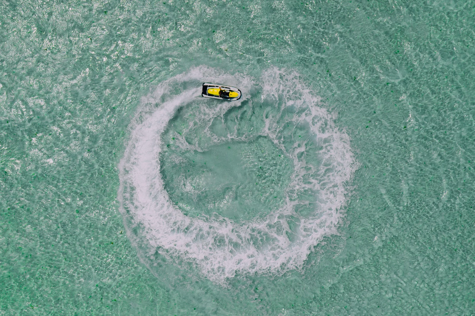 Vue aérienne d’un jet ski dessinant un cercle d’écume dans une eau turquoise