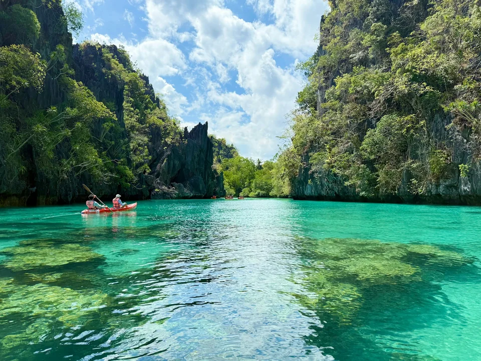 Deux personnes en kayak sur une eau turquoise entre des falaises tropicales